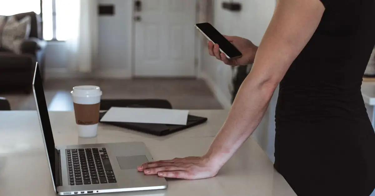 Eine Frau in einem schwarzen Kleid berechnet mit Laptop und Handy prüft ihre Rentenpunkte.