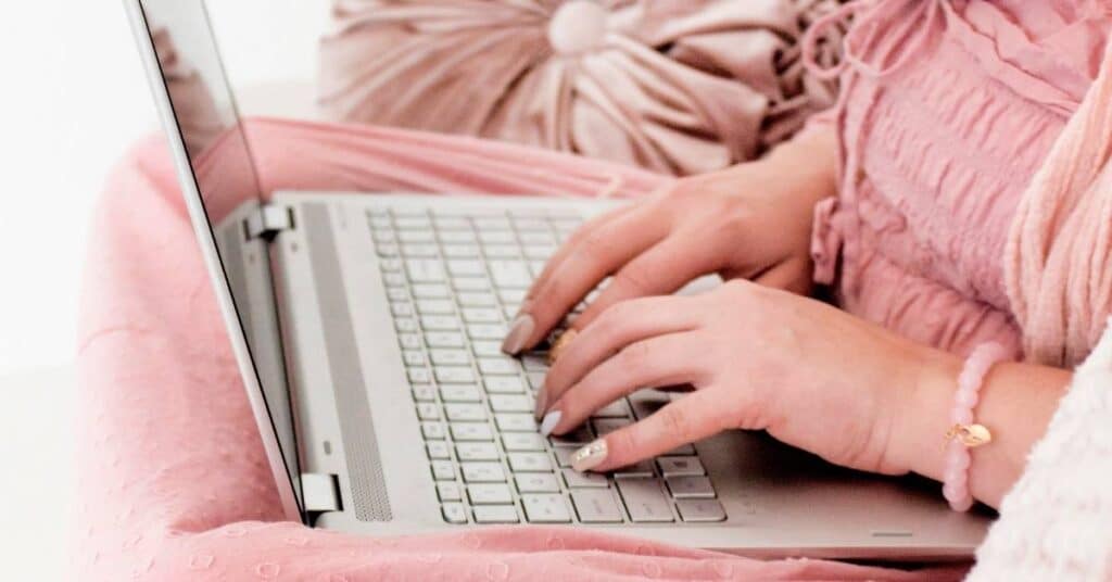 Hände tippen auf einem Laptop in einer gemütlichen rosa Umgebung.