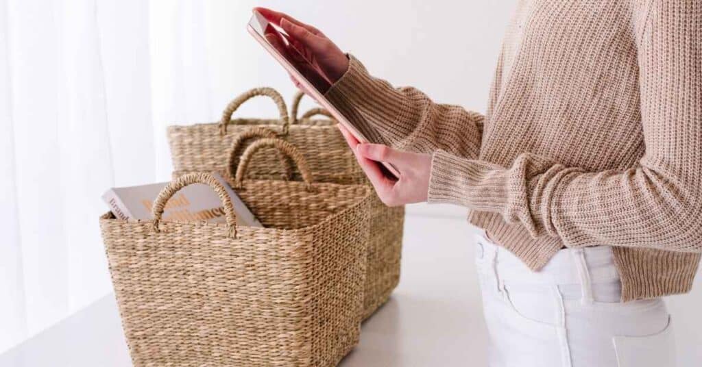 Person, die ein Tablet neben geflochtenen Körben auf einem Tisch hält.