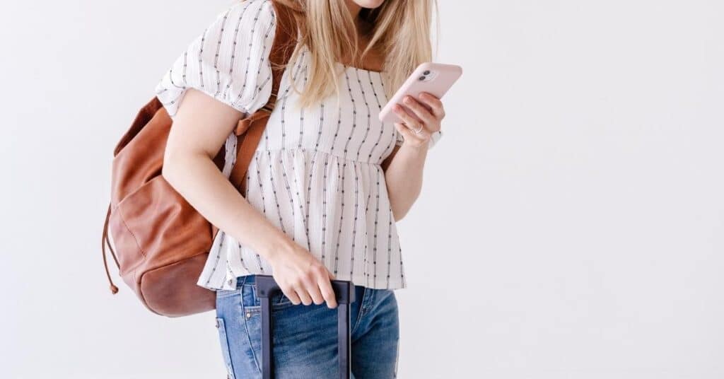 Person mit Rucksack und Koffer checkt ihr Telefon.