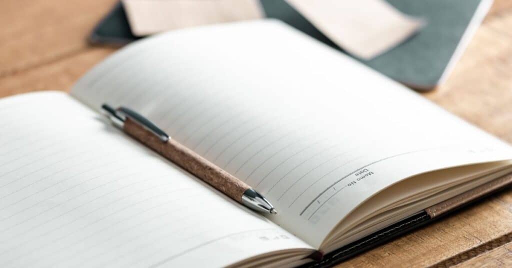 Ein aufgeschlagenes liniertes Notizbuch mit einem braunen Stift darauf, auf einem Holztisch platziert.