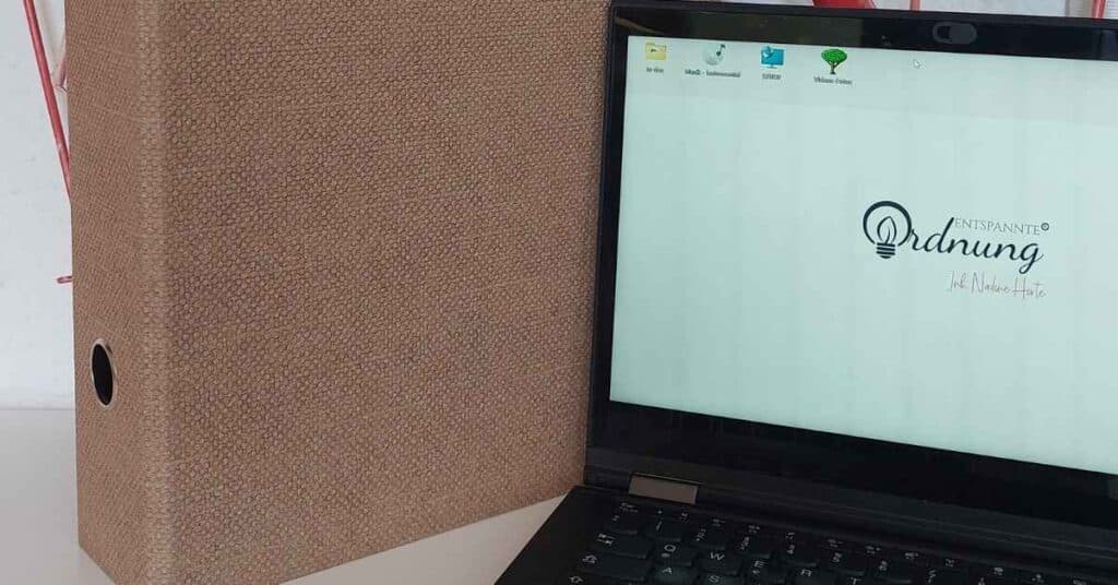 Ein Laptop mit einem Desktop-Bildschirm steht neben einem strukturierten beigen Ordner.