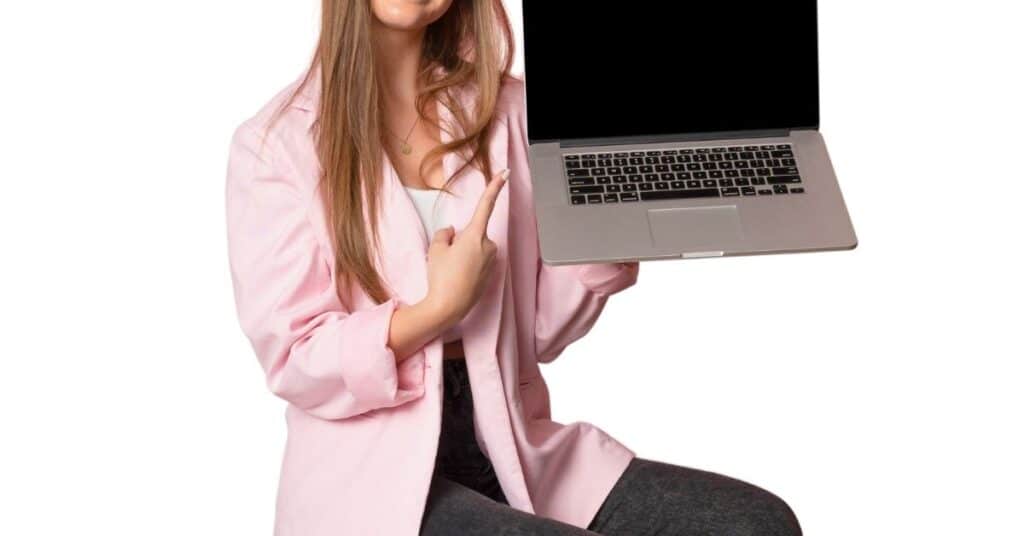 Person im rosa Blazer, die einen geöffneten Laptop mit leerem Bildschirm hält und darauf zeigt.